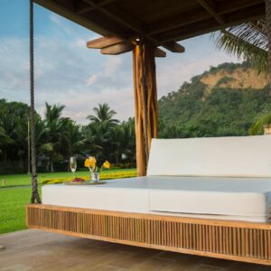 A luxurious swing bed under a wooden canopy with tropical palm trees.